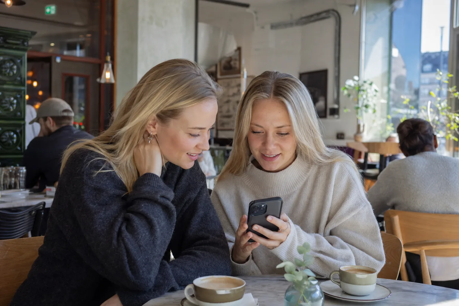 Två vänner använder smartphones på café